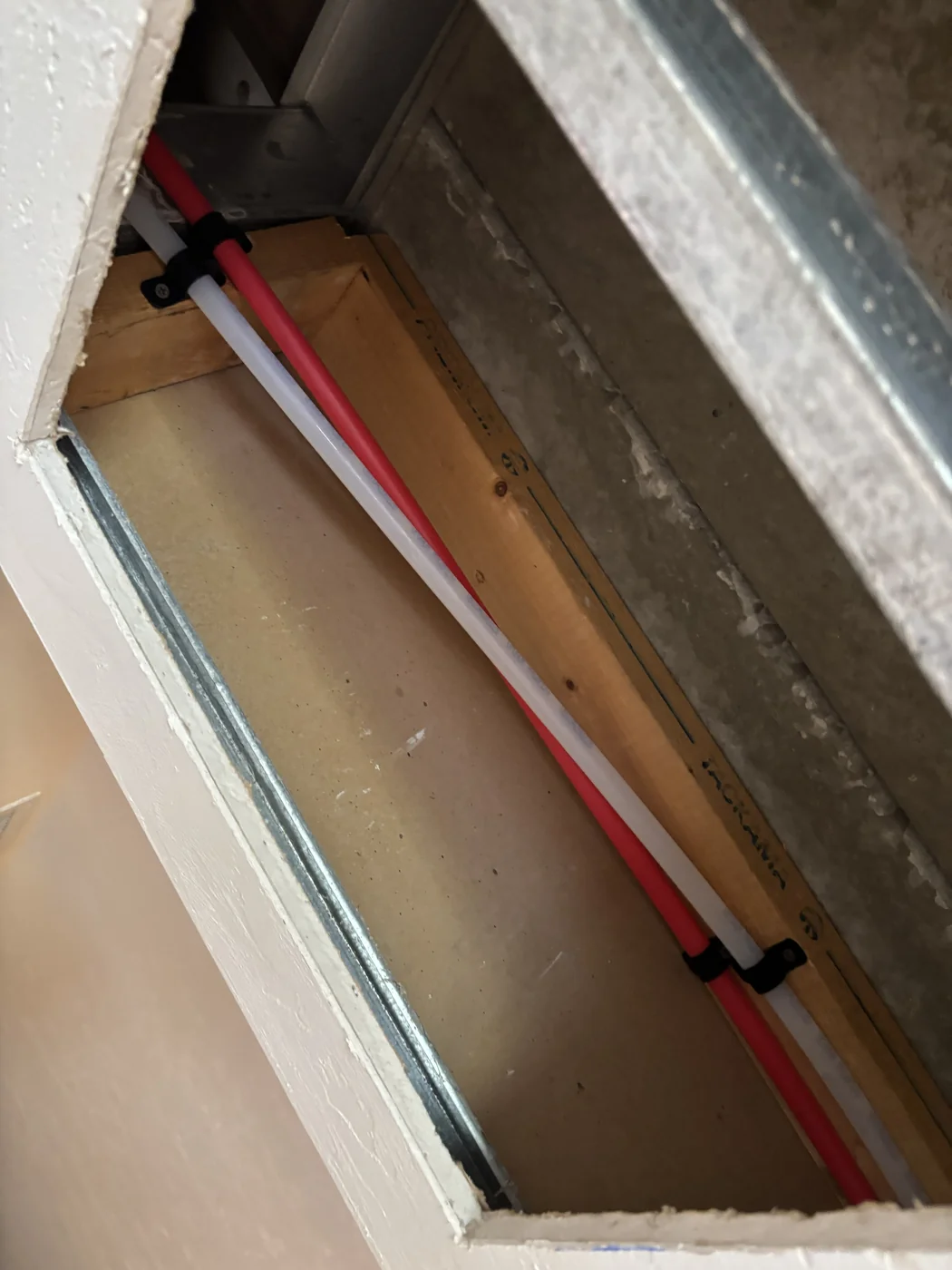 Red and white supply pipes secured inside an opened wall cavity
